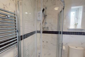 A modern bathroom with a glass-enclosed shower, a chrome towel rack, a marble-tiled floor, and a white toilet. - Apartment 101 - Symons House (Medway)