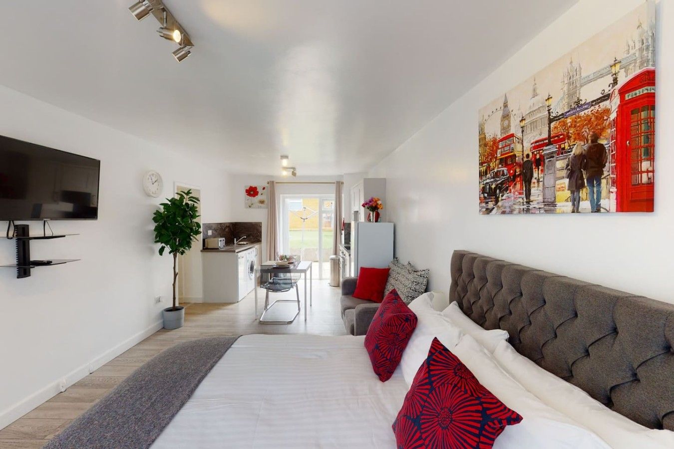 A modern hotel room with a large bed, a flat-screen TV, a kitchenette, and a dining area.