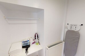A bathroom with a white radiator, a towel rack, a shelf with toiletries, and an iron. - Apartment 101 - Symons House (Medway)