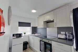 A compact kitchen with white cabinets, a microwave, a sink, and a coffee maker. - Apartment 203 - Symons House (Medway)