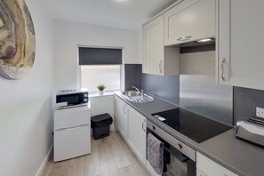 A compact kitchen with a microwave, oven, and sink. - Apartment 203 - Symons House (Medway)
