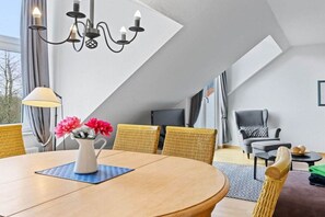 Ein modernes Wohnzimmer mit einem runden Holztisch, Korbstühlen, einem grauen Sofa und einem schwarzen Sessel.