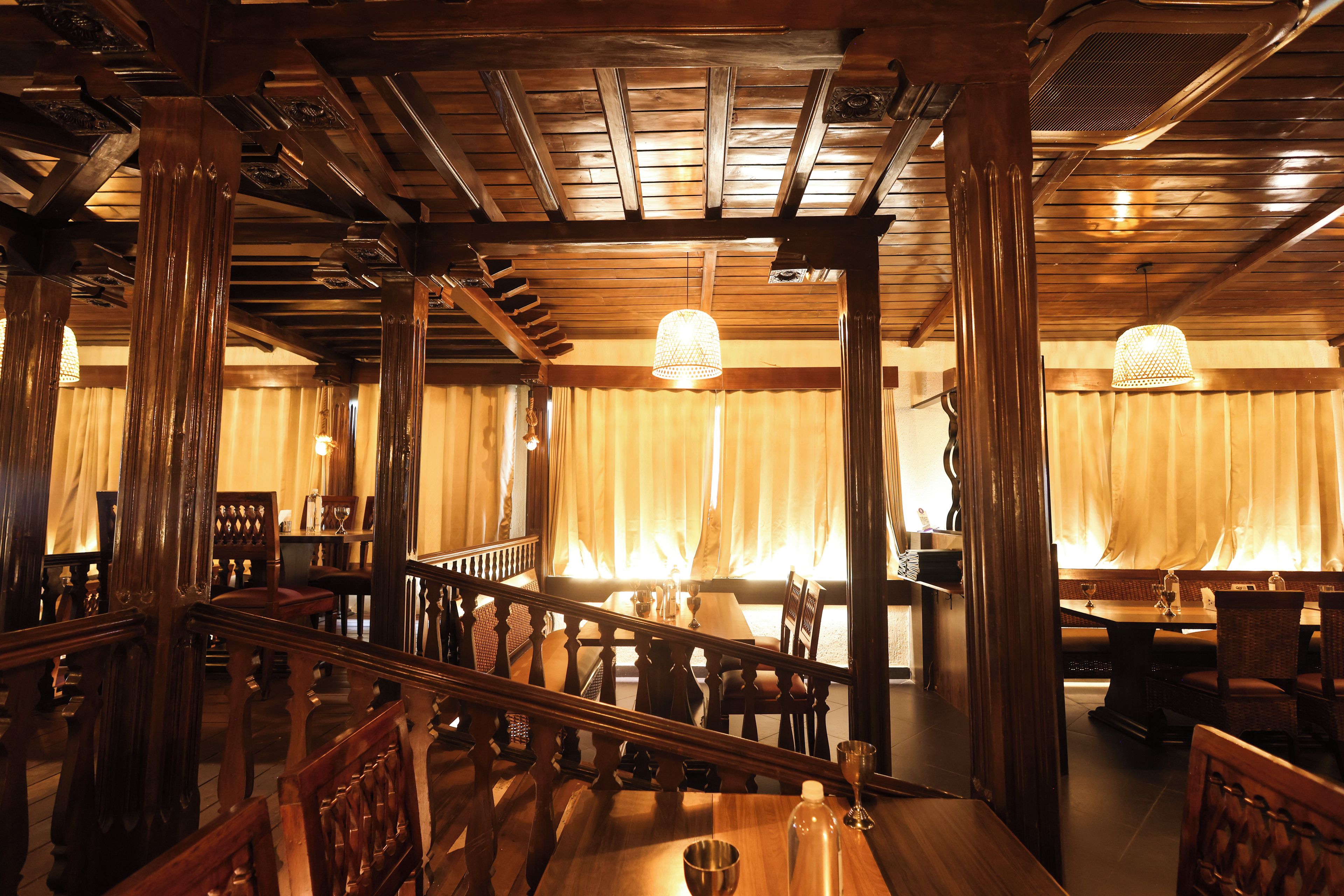 Interior de restaurante con vigas de madera, una escalera y mesas dispuestas para comer.