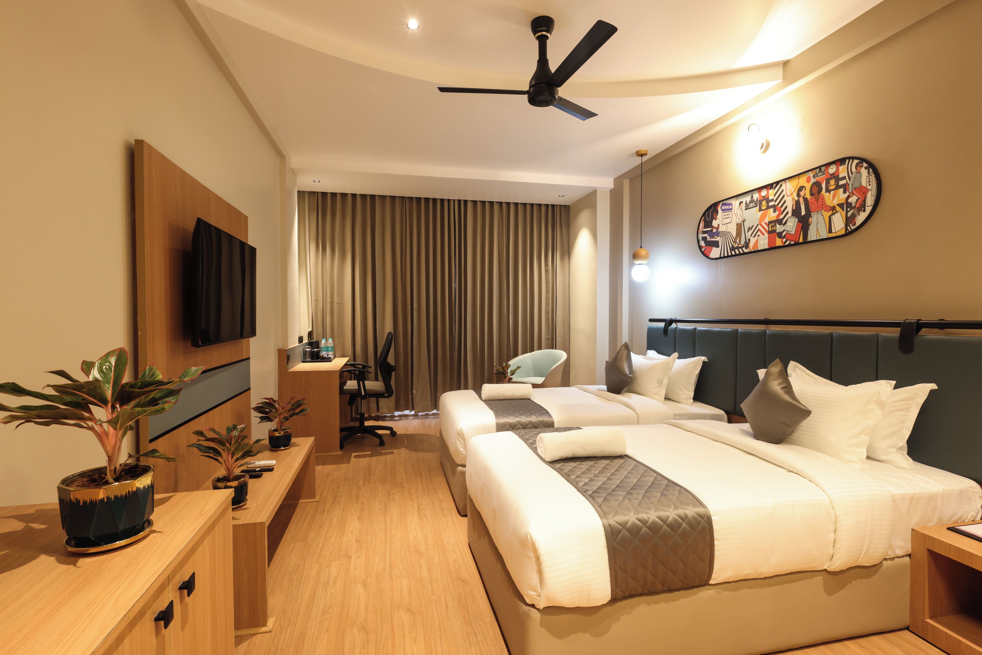 Habitación de hotel con dos camas, un escritorio, una silla, un televisor y un ventilador de techo.