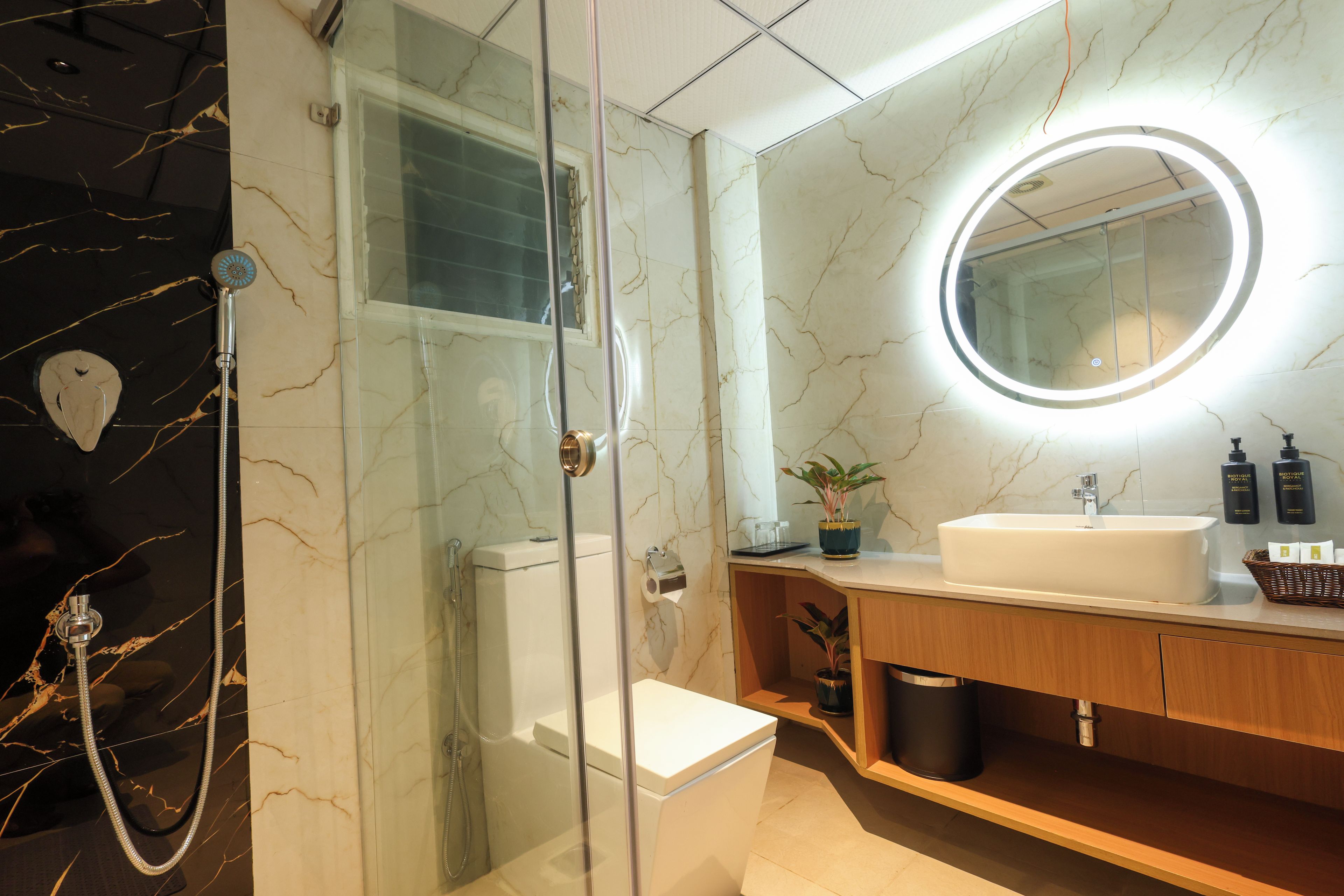 Une salle de bain moderne avec une douche à parois de verre, des toilettes blanches, un meuble-lavabo et un miroir doté d’un éclairage circulaire.