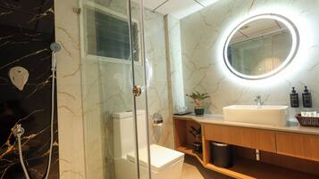 Une salle de bain moderne avec une douche à parois de verre, des toilettes blanches, un meuble-lavabo et un miroir doté d’un éclairage circulaire.