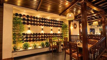 Interior de restaurante com uma parede de pratos decorativos, vigas de madeira no teto e uma escadaria.
