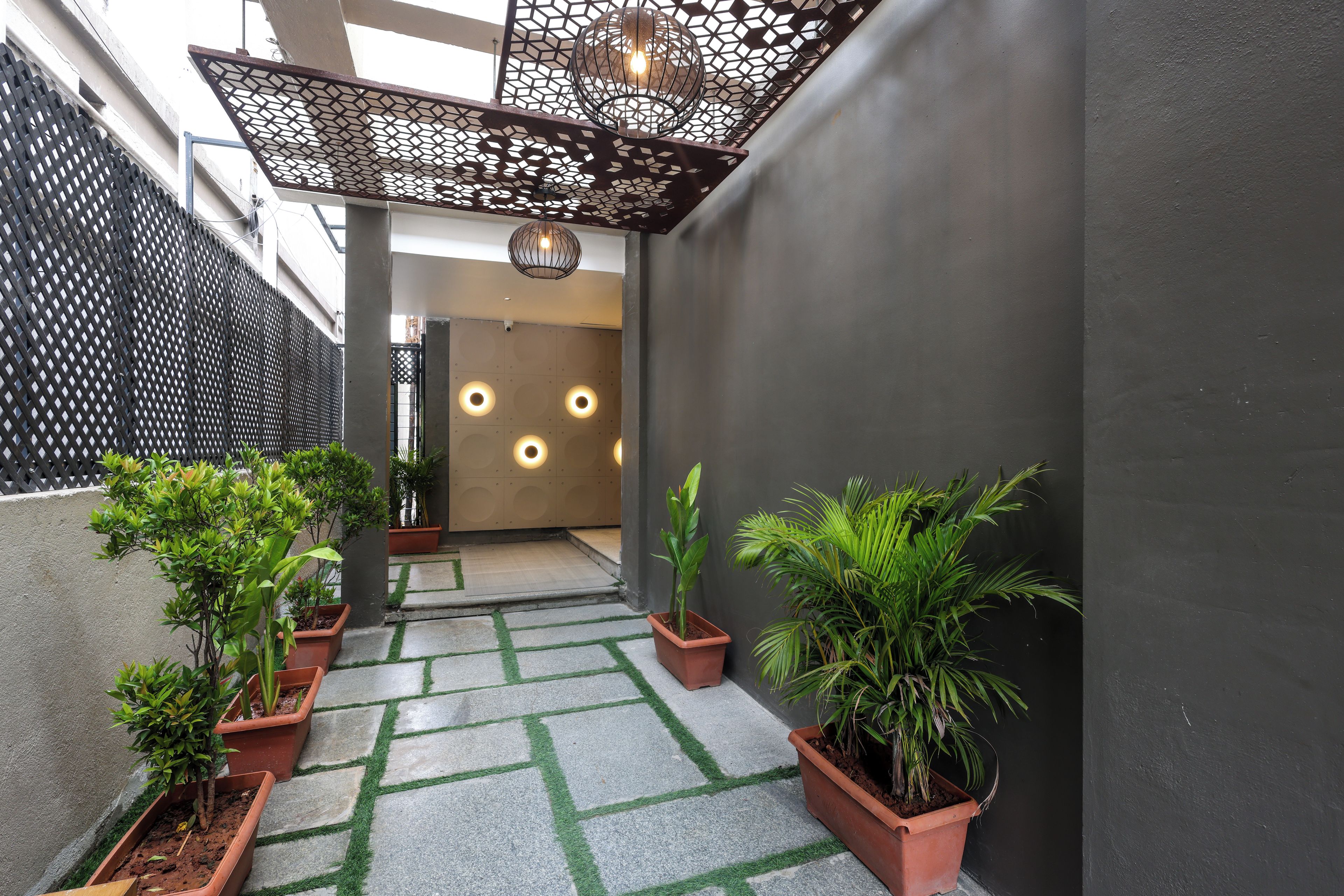 A narrow outdoor corridor with potted plants, a geometric patterned floor, and a modern light fixture.