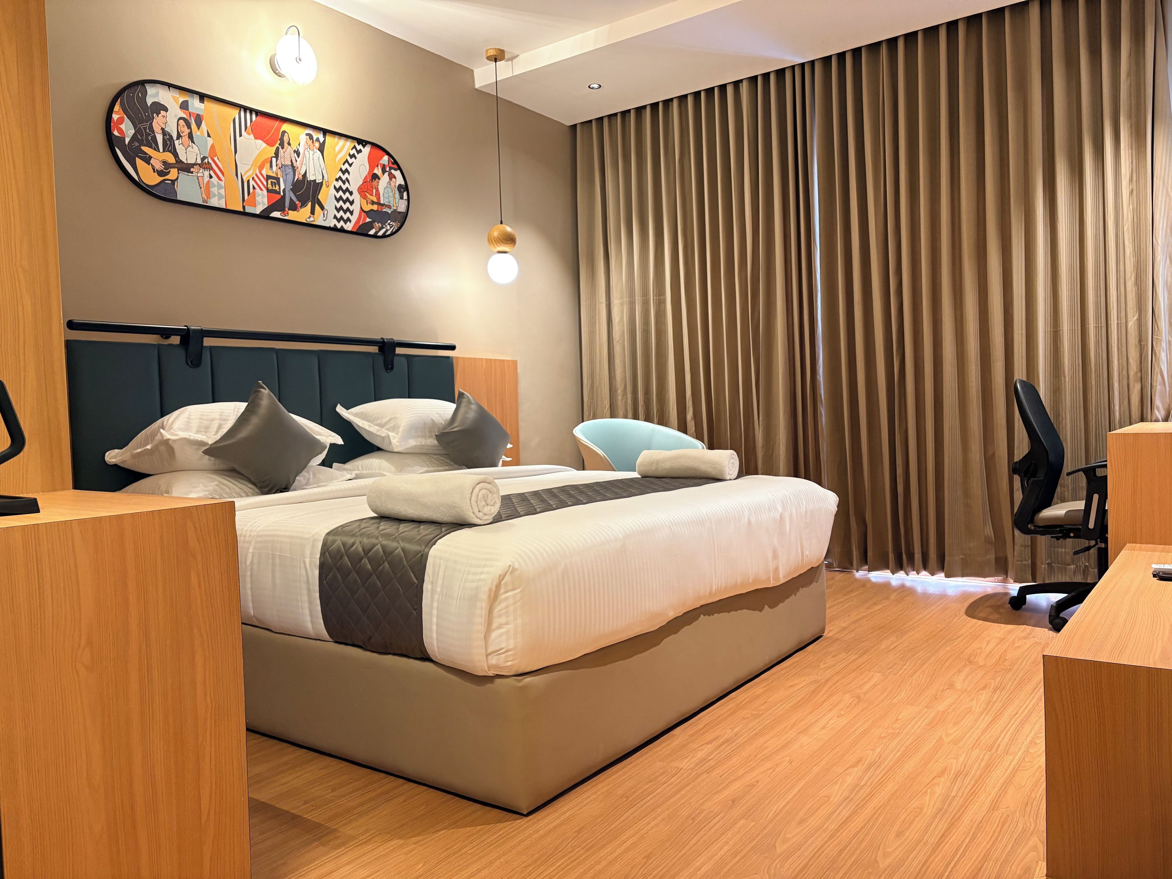 Een moderne hotelkamer met een groot bed, een bureau, een stoel, een hoofdbord, een kunstwerk aan de muur en een gordijn.