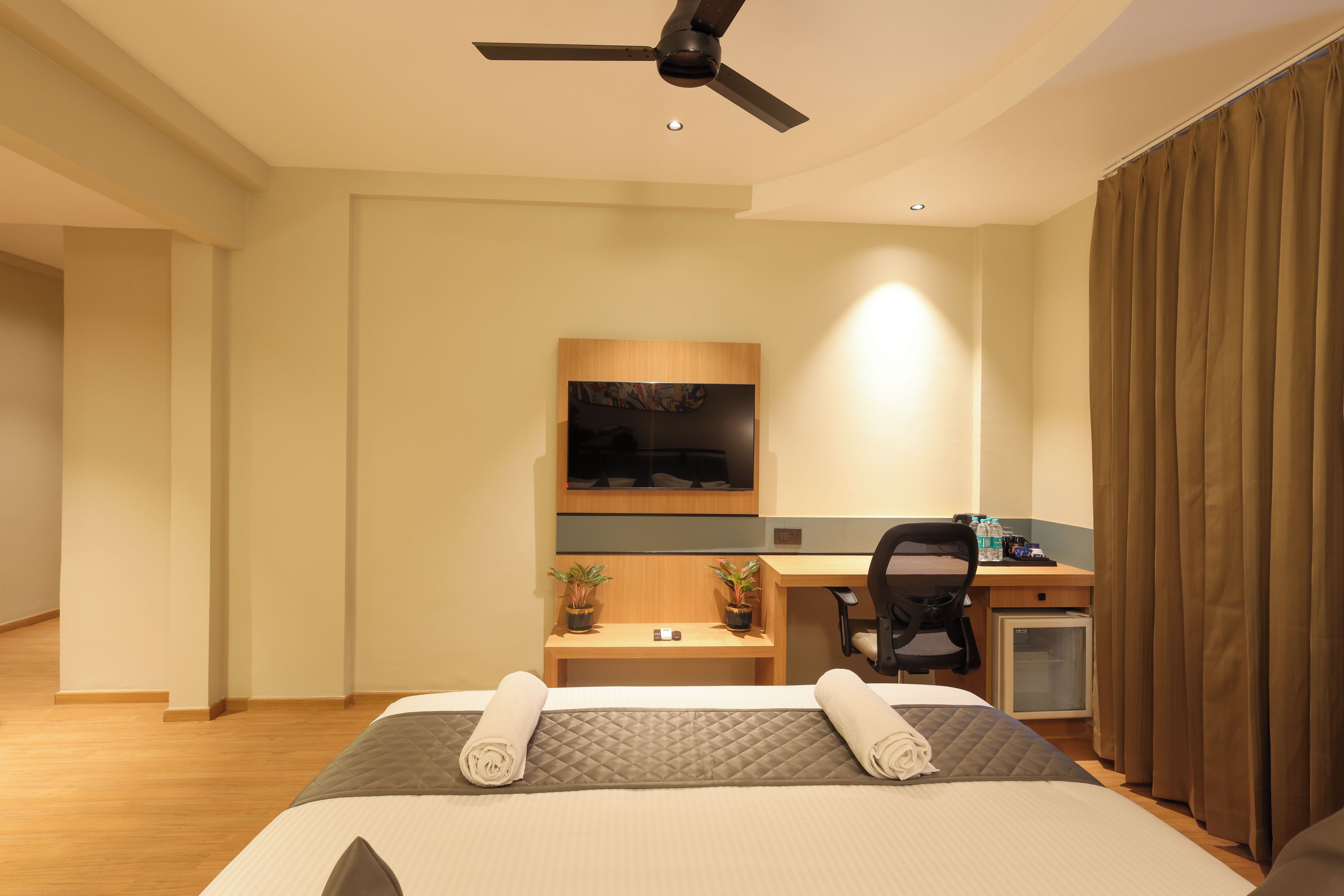 A hotel room with a bed, a desk, a chair, a television, and a ceiling fan.