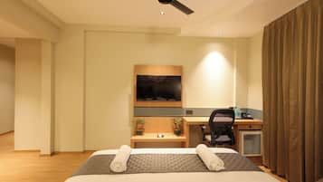 Ein Hotelzimmer mit Bett, Schreibtisch, Sessel, Fernseher und Deckenventilator.