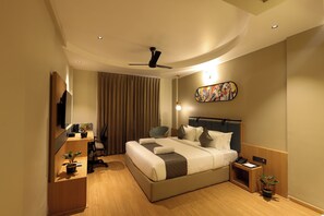 Habitación de hotel moderna con una cama grande, un escritorio, una silla, un ventilador de techo y un televisor instalado en la pared.
