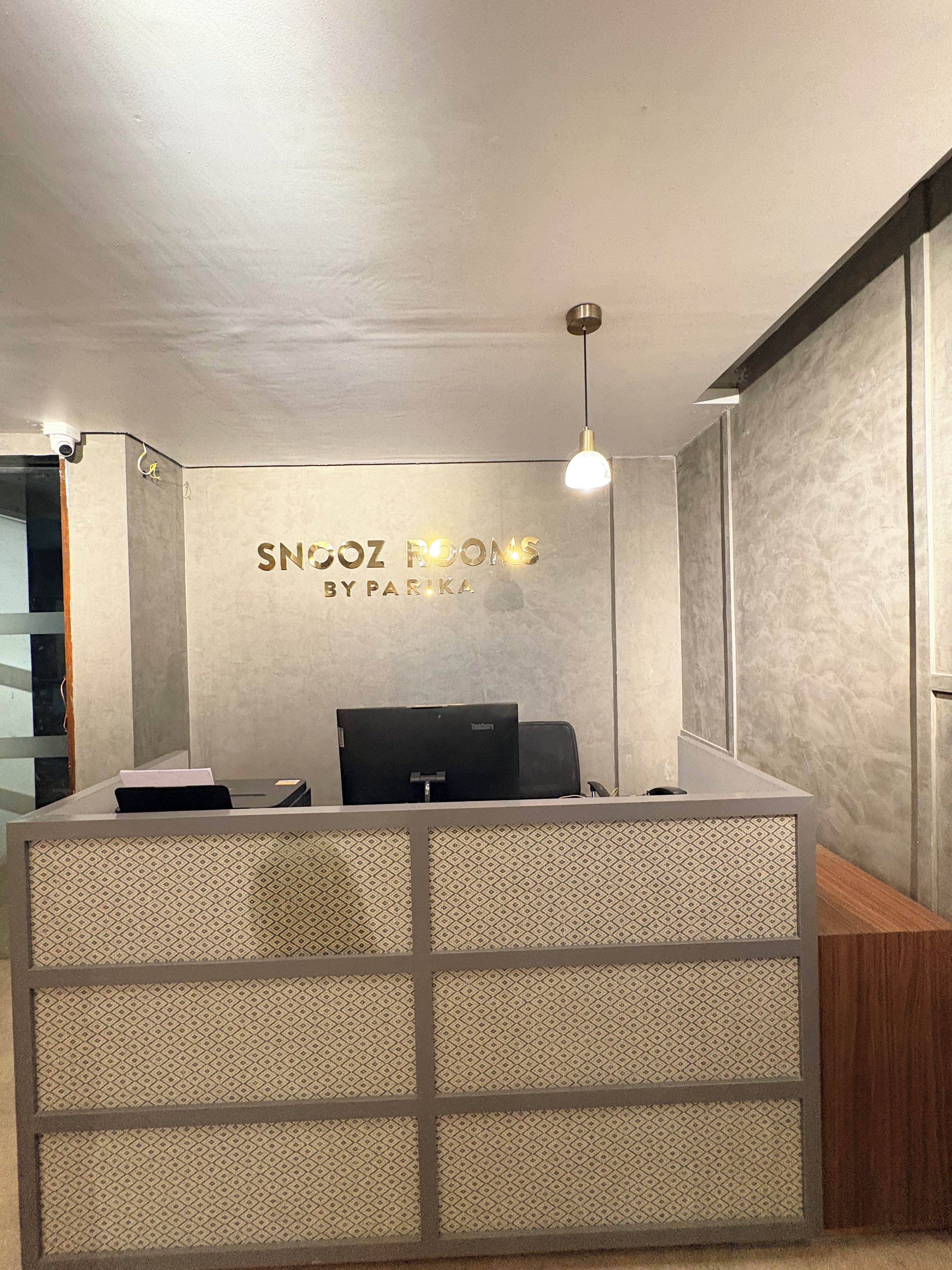 Een receptiebalie met een gedeeltelijk gescheiden wand, een computer aan de muur en een hanglamp.