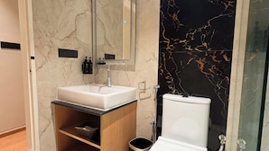 A modern bathroom with a white toilet, a vanity with a mirror, and a shower area. - Snooz Rooms By Parika A VYDA Hotel (Bengaluru)