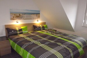 A bedroom with a bed, two pillows, a headboard, and a painting on the wall. - Holiday home with 2 bedrooms (Carolinensiel)
