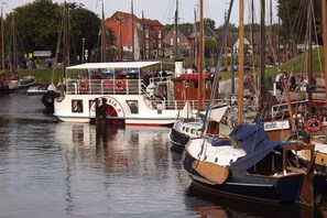 A marina with various boats docked, including a white boat with a covered deck and a smaller boat with a blue tarp. - Holiday home with 2 bedrooms (Carolinensiel)