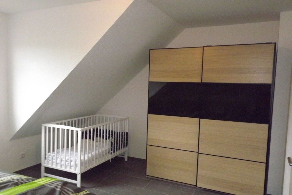 A room with a sloped ceiling, a white crib, and a cabinet with multiple compartments.