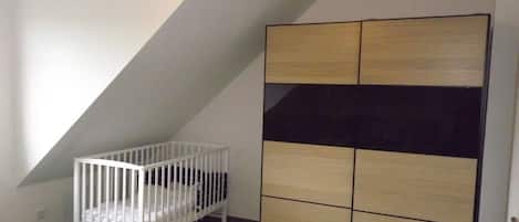 Una habitación con techo inclinado, una cuna blanca y un armario con varios compartimentos.