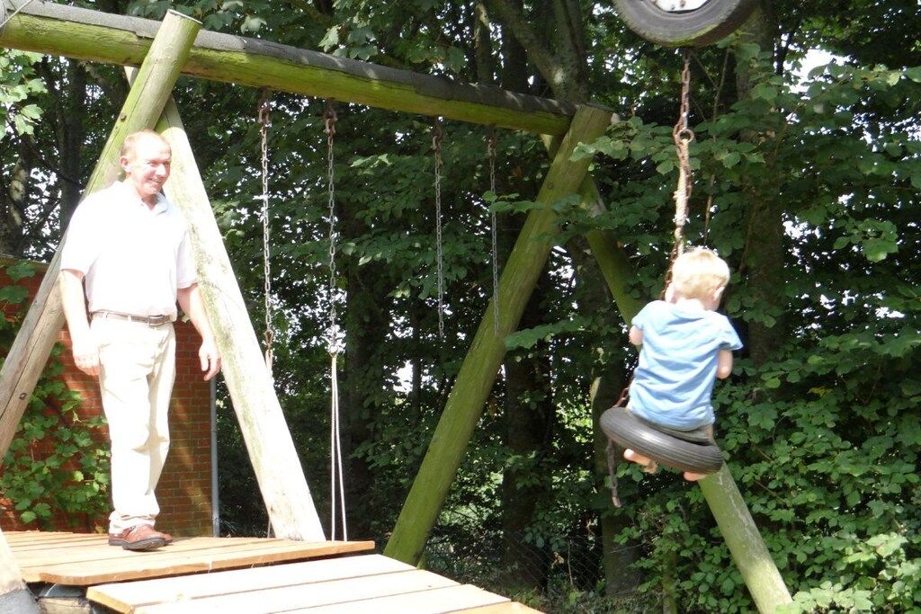 Une balançoire en bois avec un siège en forme de pneu, entourée de verdure.