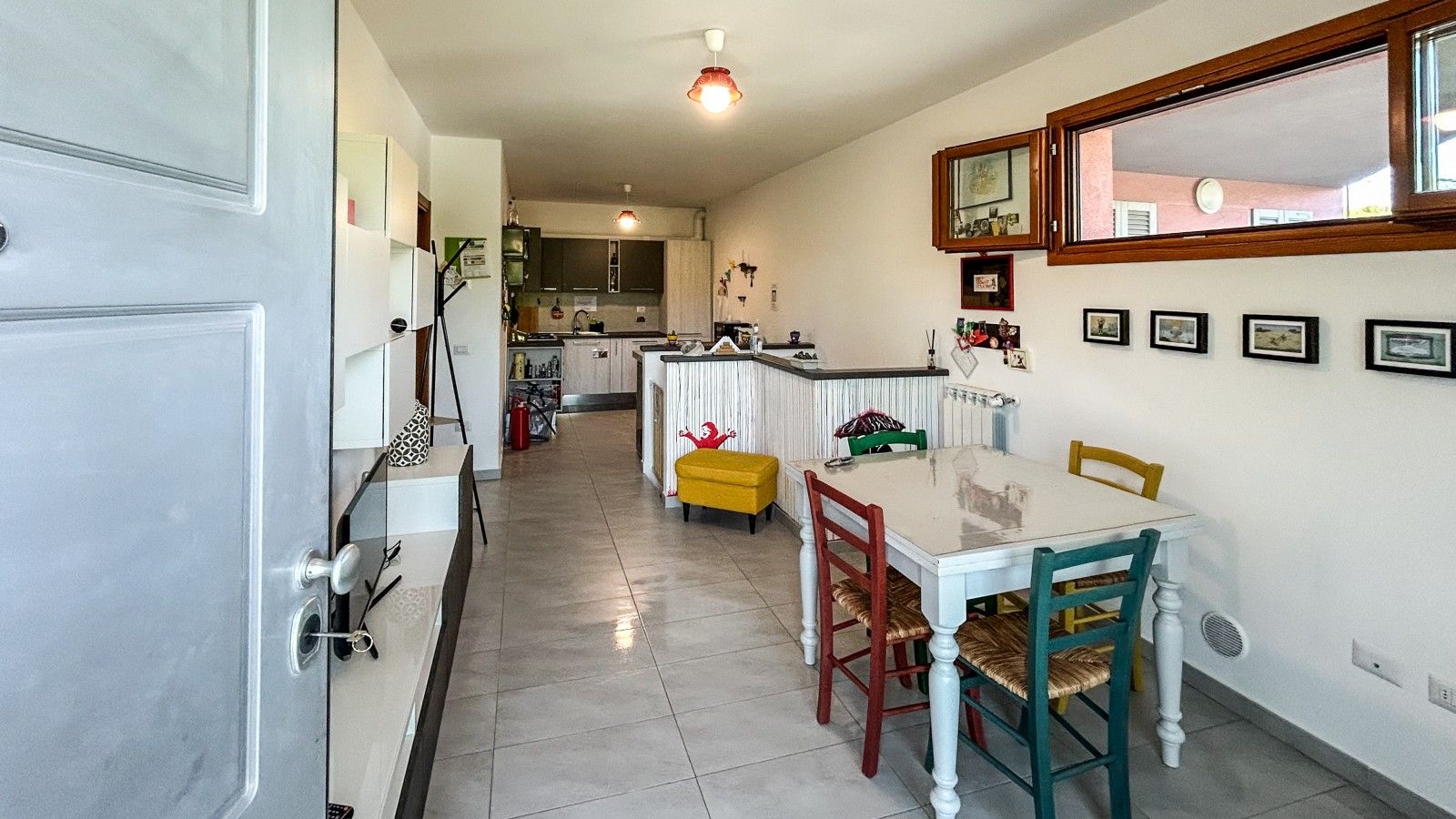 Un coin repas avec une table et des chaises, une cuisine en arrière-plan et une porte sur la gauche.