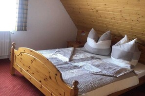 Ein hölzernes Bett mit Kopfteil, ein Fenster mit Vorhang und ein kleiner Nachttisch mit Lampe.