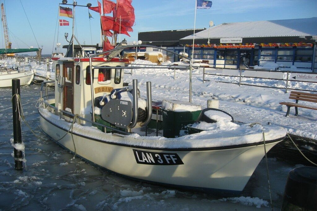 A boat docked at a harbor with a snow-covered pier and a building in the background.