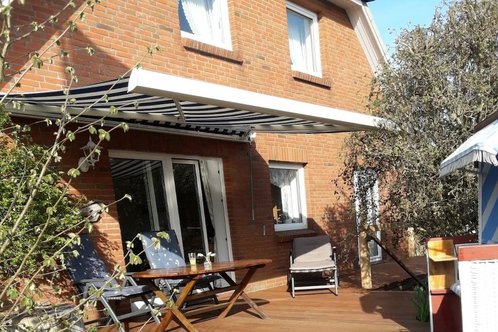 Une maison en briques dotée d’un patio comprenant une table et des chaises, un espace salon couvert et une porte-fenêtre coulissante.