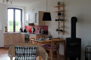 A kitchen with wooden cabinets, a stove, and a dining area with a wicker chair. - Holiday apartment with 1 bedroom (Büschow)