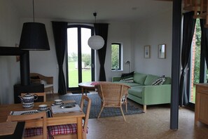 Ein Wohnzimmer mit einem grünen Sofa, einem Esstisch mit Teekanne und einem großen Fenster mit Vorhängen.