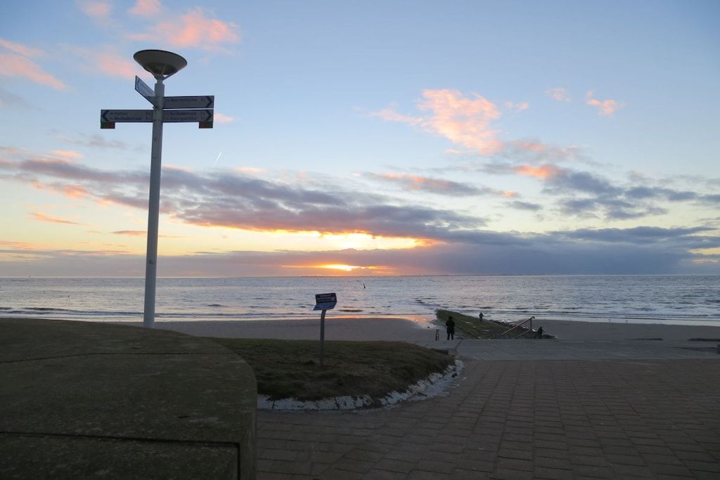 A sunset view from a paved walkway with a street lamp and directional sign.