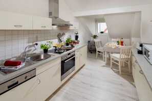 A modern kitchen with a built-in oven, a sink, and a dining area with a table and chairs. - Holiday apartment with 1 bedroom (Norderney)
