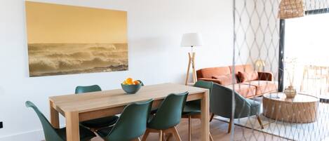 A dining area with a wooden table and chairs, a bowl of fruit, and a painting on the wall.