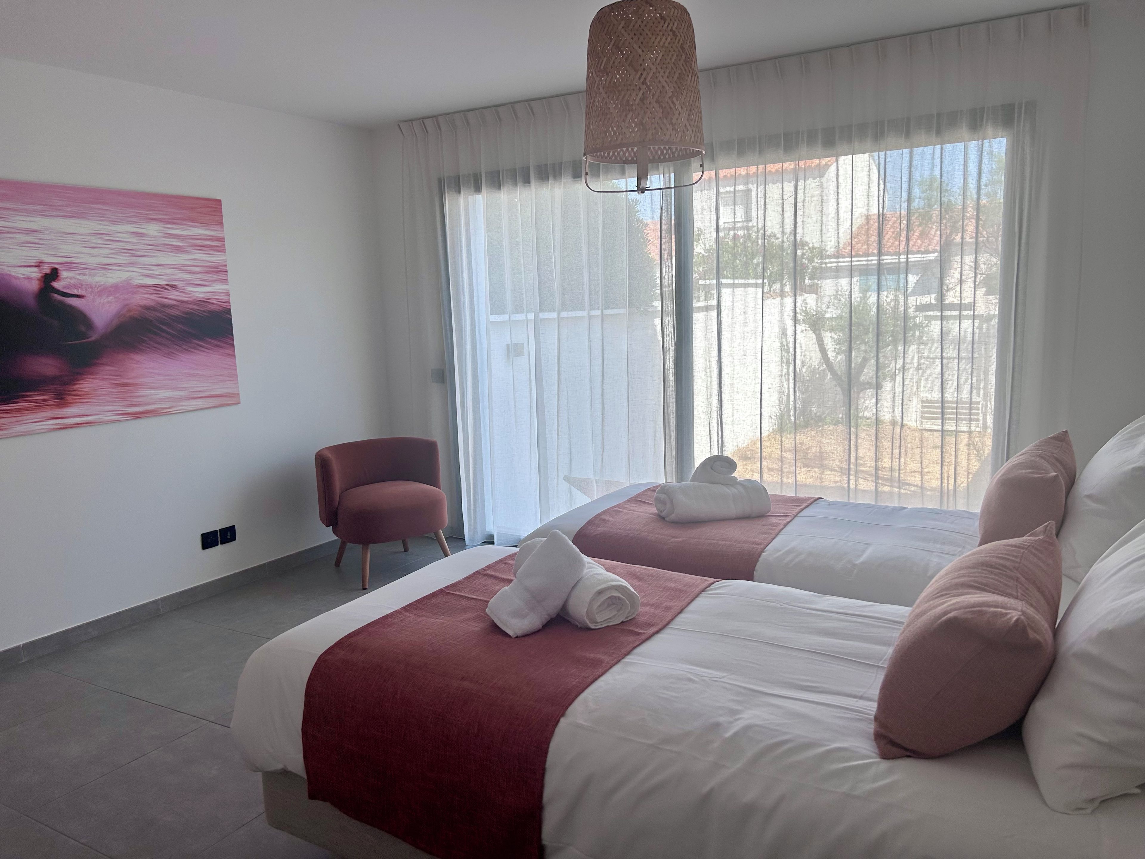 Een hotelkamer met twee bedden, een stoel, een schilderij en een groot raam.