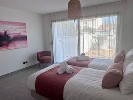 Habitación de hotel con dos camas, una silla, un cuadro y un ventanal grande.