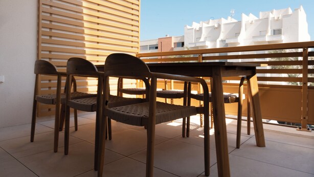 Un balcón con una mesa y cuatro sillas, con vista a un edificio de fachada blanca.