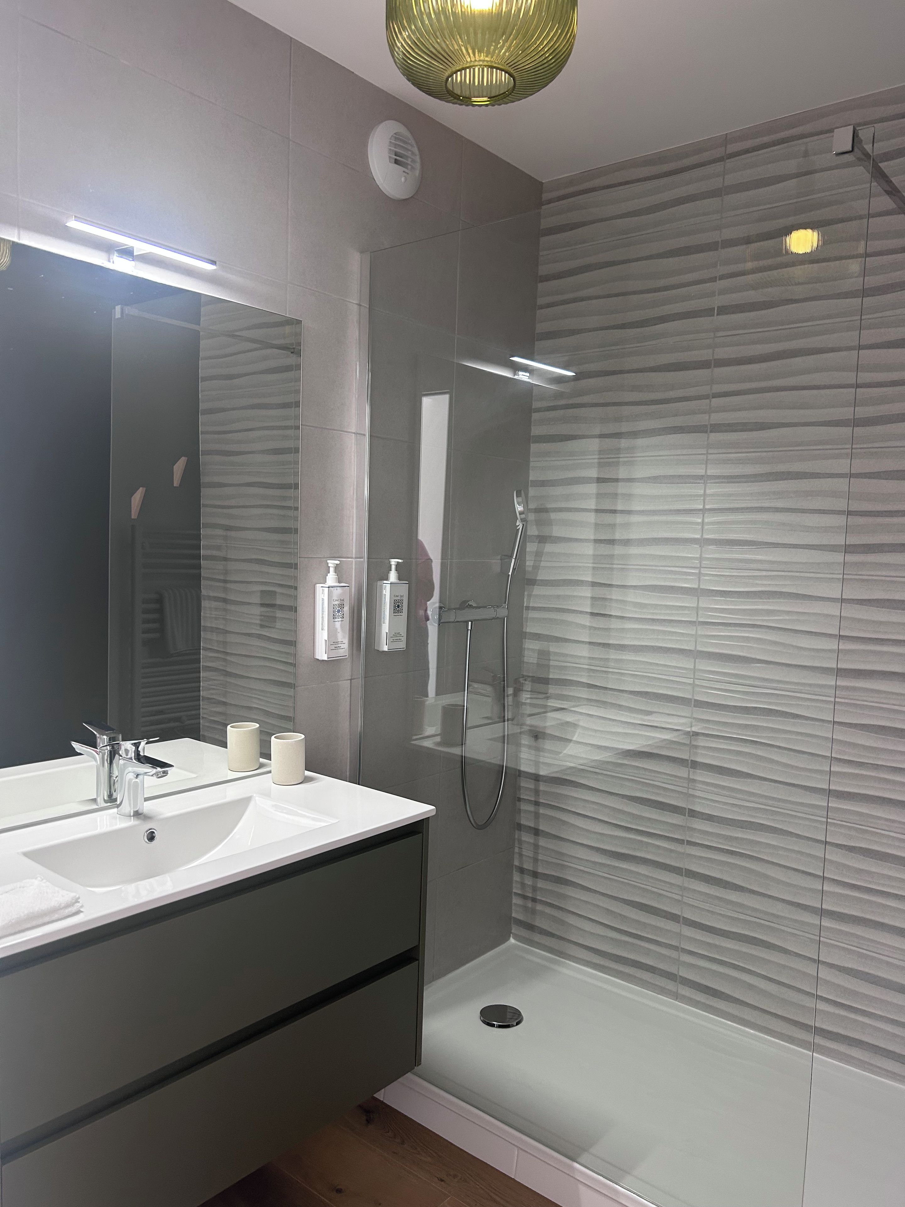 Een moderne badkamer met een wastafel met twee wasbakken, een grote spiegel, een handdouche en een douche met glazen wanden.