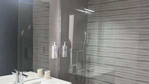 Un baño moderno con tocador de doble lavabo, un espejo grande, cabezal de ducha manual y ducha con mampara de vidrio.