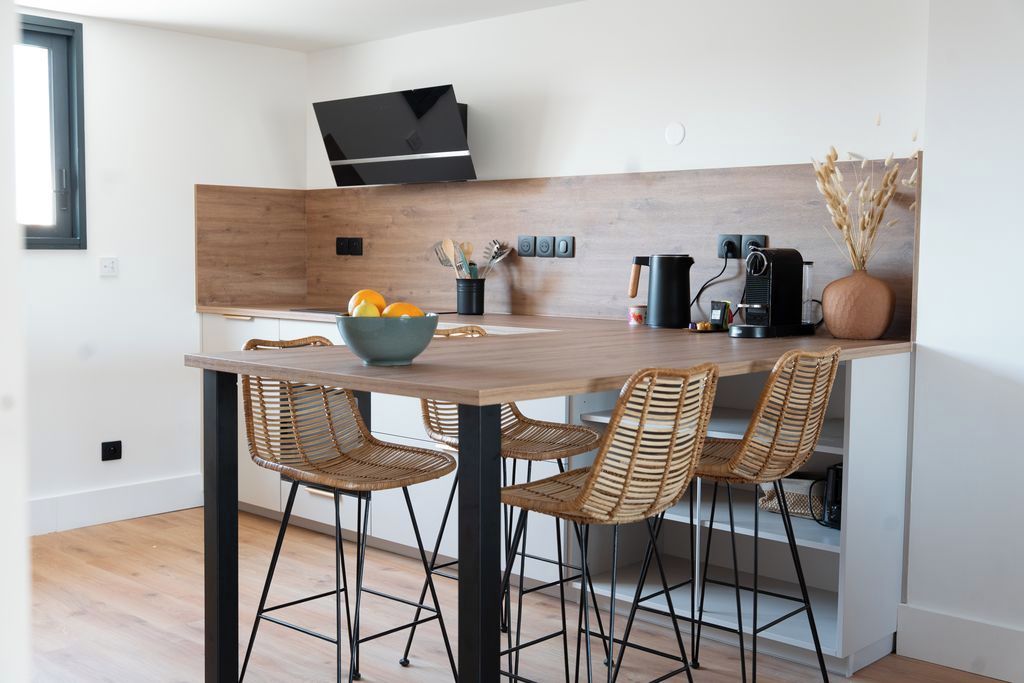Een moderne keuken met een houten aanrecht, vier rieten stoelen, een fruitschaal en een koffiezetapparaat.