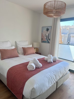 Habitación de hotel con una cama grande, ropa de cama blanca y una manta roja, y vistas de edificios.