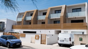Un edificio moderno de varios pisos con balcones, un área de estacionamiento y un cartel que indica una oficina de turismo.