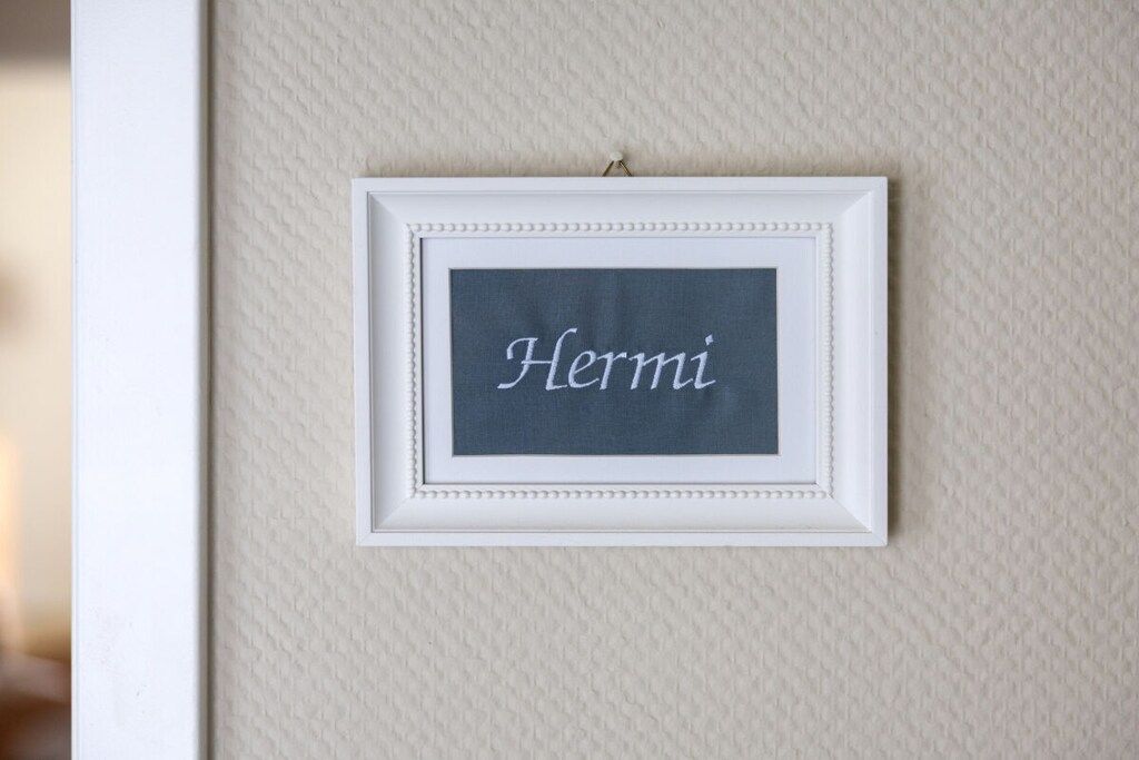 Ein gerahmtes Schild mit dem Namen 'Hermi' an einer strukturierten Wand.
