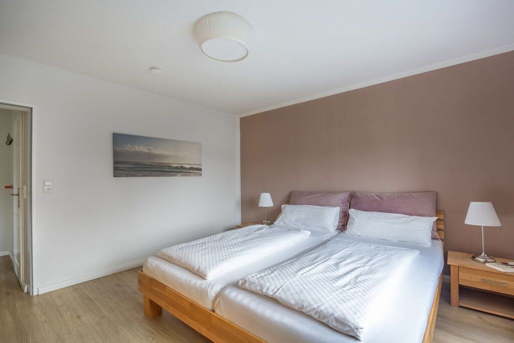 A bedroom with a bed, bedside lamps, a painting on the wall, and a door.