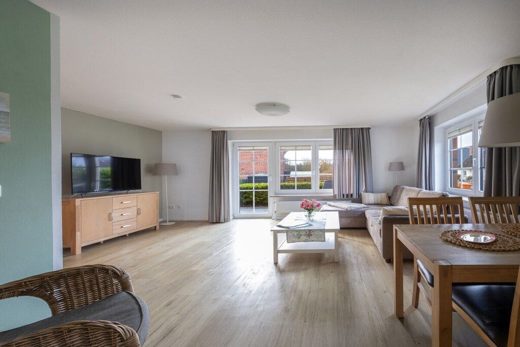 A modern living room with a television, sofa, dining table, and a view of the outside.