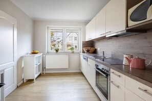 Eine kleine Küche mit Fenster, weißen Schränken und einer Mikrowelle.