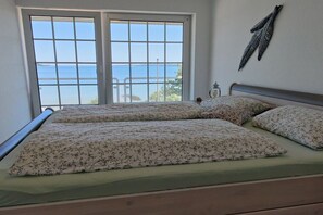 A bed with floral bedding, a view of the sea through a large window, and a decorative wall piece. - Holiday apartment in Harrislee with Wi-Fi (Harrislee)