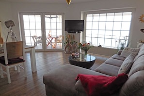A living room with a sofa, a coffee table, a TV, and a balcony with a table and chairs. - Holiday apartment in Harrislee with Wi-Fi (Harrislee)