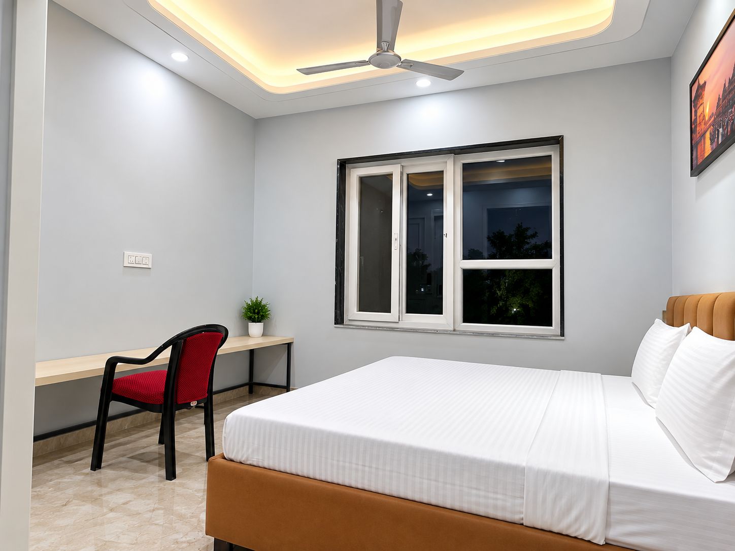 A bedroom with a bed, a desk, a chair, a window, and a ceiling fan.