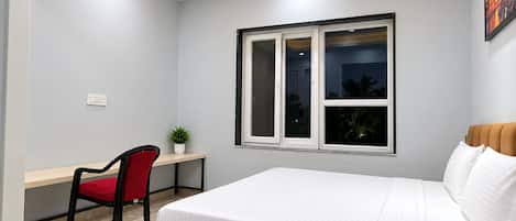 Ein Schlafzimmer mit Bett, Schreibtisch, Stuhl, Fenster und Deckenventilator.