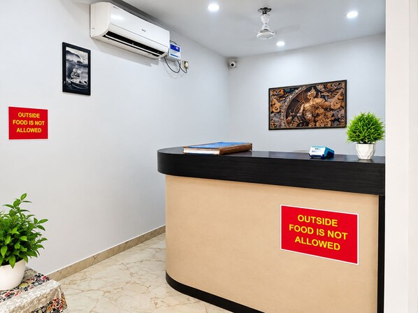 A reception desk with a 'Outside Food is Not Allowed' sign, a framed picture, and a potted plant.