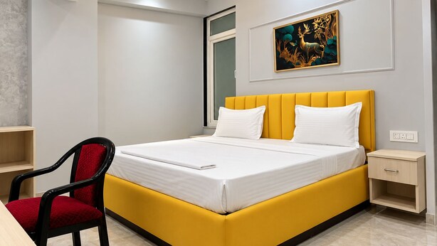 A modern bedroom with a yellow bed, white pillows, a red chair, a ceiling fan, and a painting on the wall.